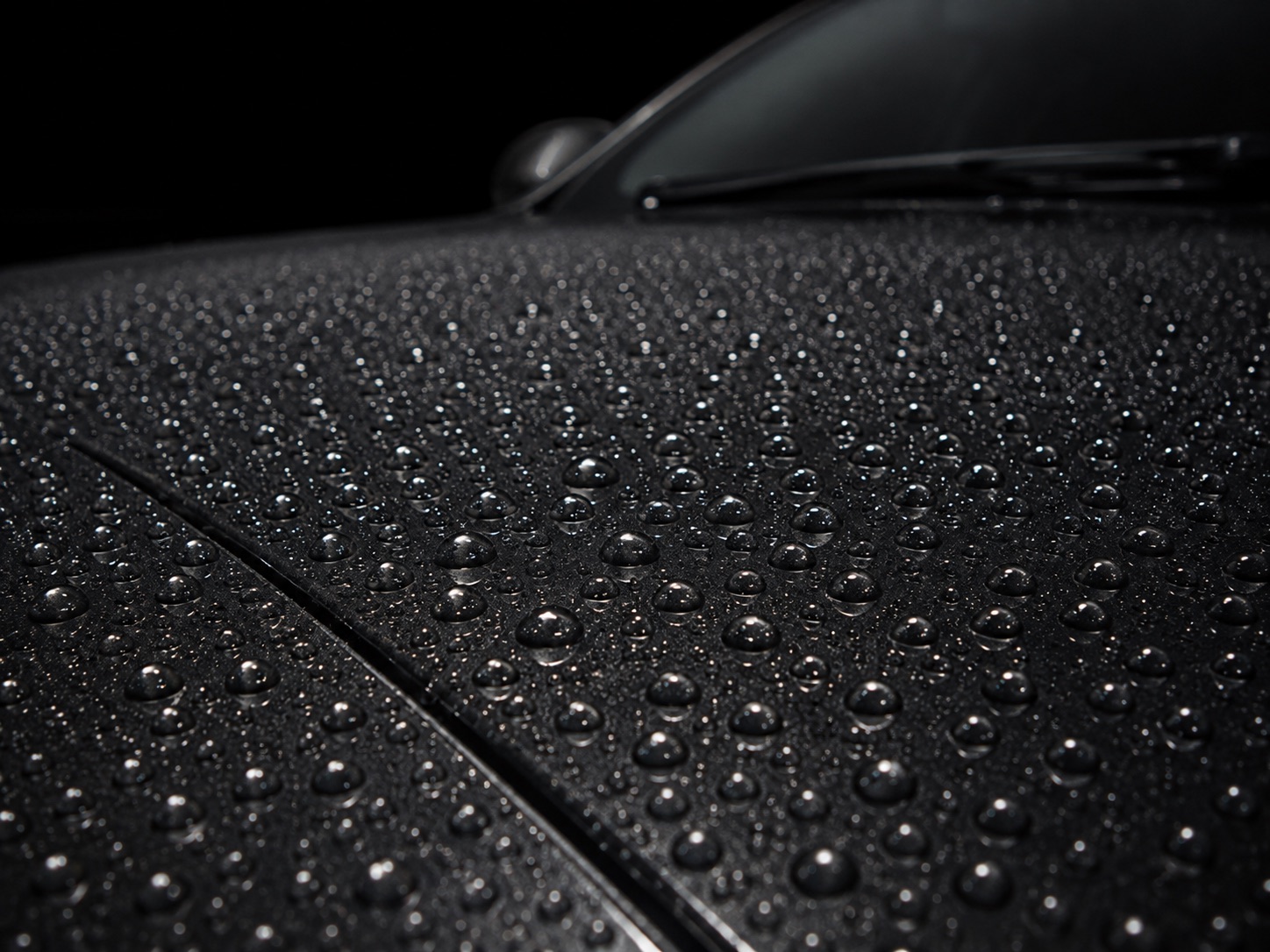 Dense, tall water beads standing on the dark glossy hood of a ceramic-coated car